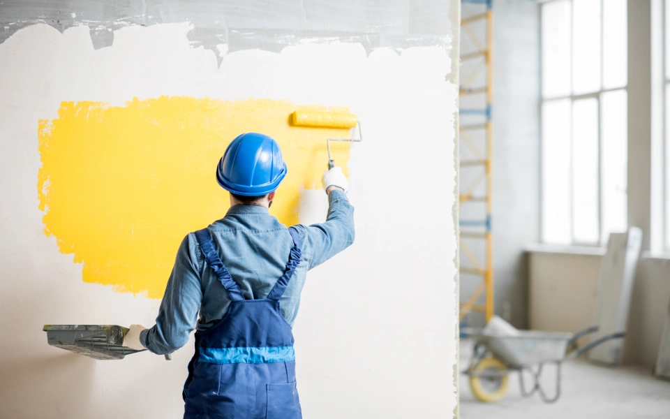 Man in blue coloring a wall with yellow